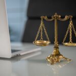 Photo of a small scales of justice placed on a desk next to a laptop