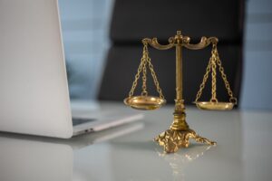 Photo of a small scales of justice placed on a desk next to a laptop