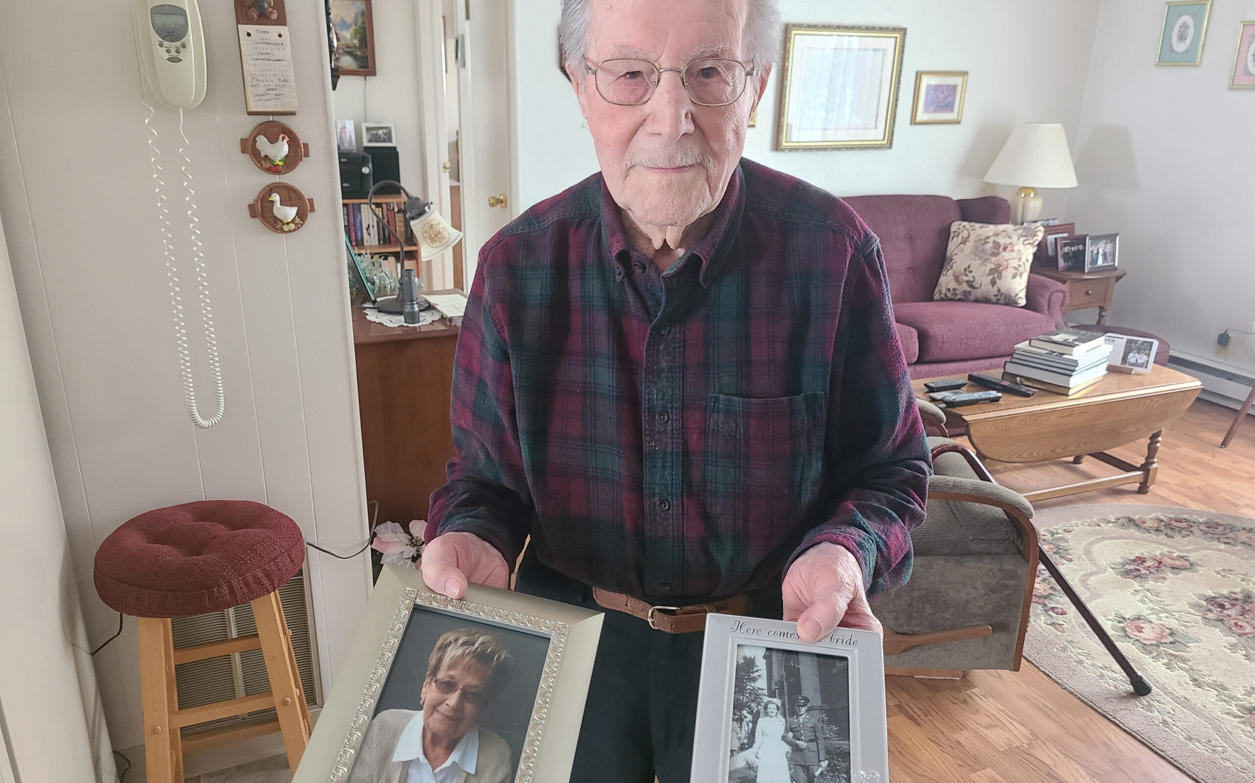 Armand Martin poses with photos of his two wives, both named Yvette in Madawaska on Feb. 11. (Emily Jerkins | St John Valley Times)